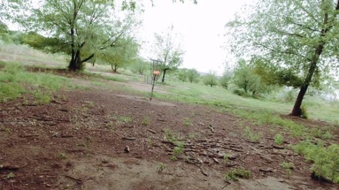 一名白人男子使用反手推杆将圆盘高尔夫推杆扔进未耕种的树木室外区域的圆盘高尔夫球篮中 (飞盘高尔夫)