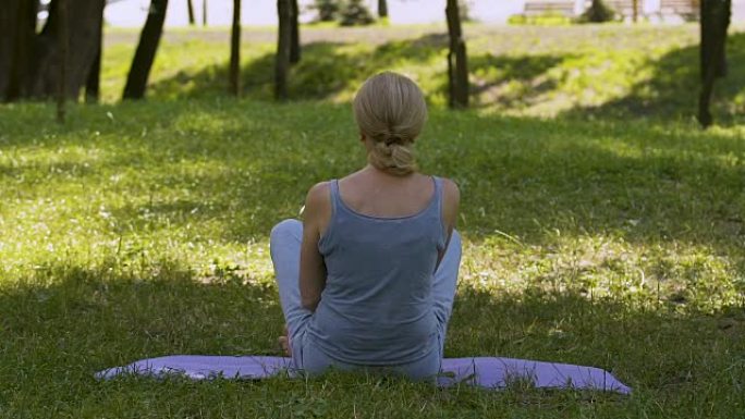 女性坐在垫子上做瑜伽体式，在公园冥想，莲花姿势，慢动作