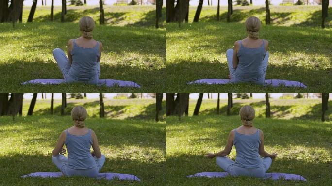 女性坐在垫子上做瑜伽体式，在公园冥想，莲花姿势，慢动作