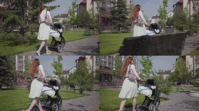 美丽的红发女人走在公园里的一条带婴儿车的石头走道上。
