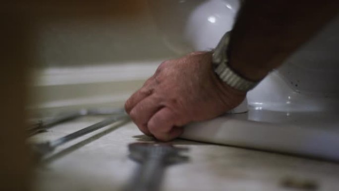 一名高加索修理工在室内家庭浴室中固定马桶时，用塑料螺栓盖覆盖了一个裸露的法兰螺栓
