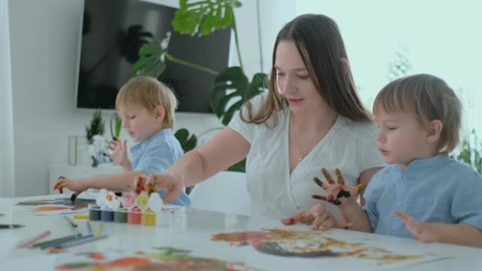 妈妈帮助她的儿子们培养创造性的技能，并与他们一起在手指的帮助下创作绘画颜料。儿童发展。创意家庭。慈爱