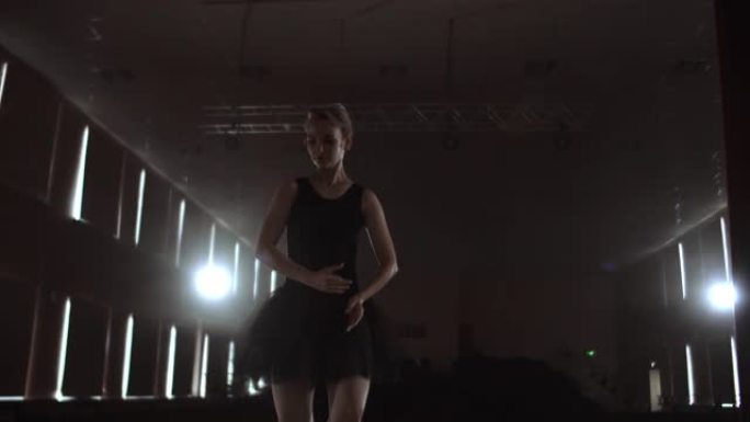 慢动作: 芭蕾舞女演员在黑暗的灯光下在舞台上的烟雾中穿着脚尖鞋跳舞。摄像机在万向节上移动。