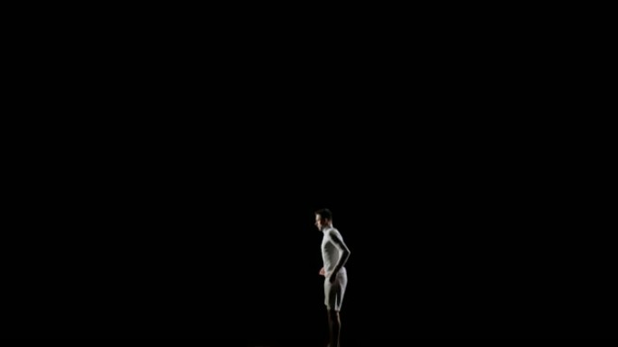 穿着黑色背景的白色衣服的英俊男性职业体操运动员在体操比赛中表演，并在蹦床跳空翻上练习