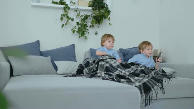 两个4岁和2岁的男孩正坐在沙发上看电视。激动人心的电视节目。查看卡通。孩子们观看激动人心的电视节目