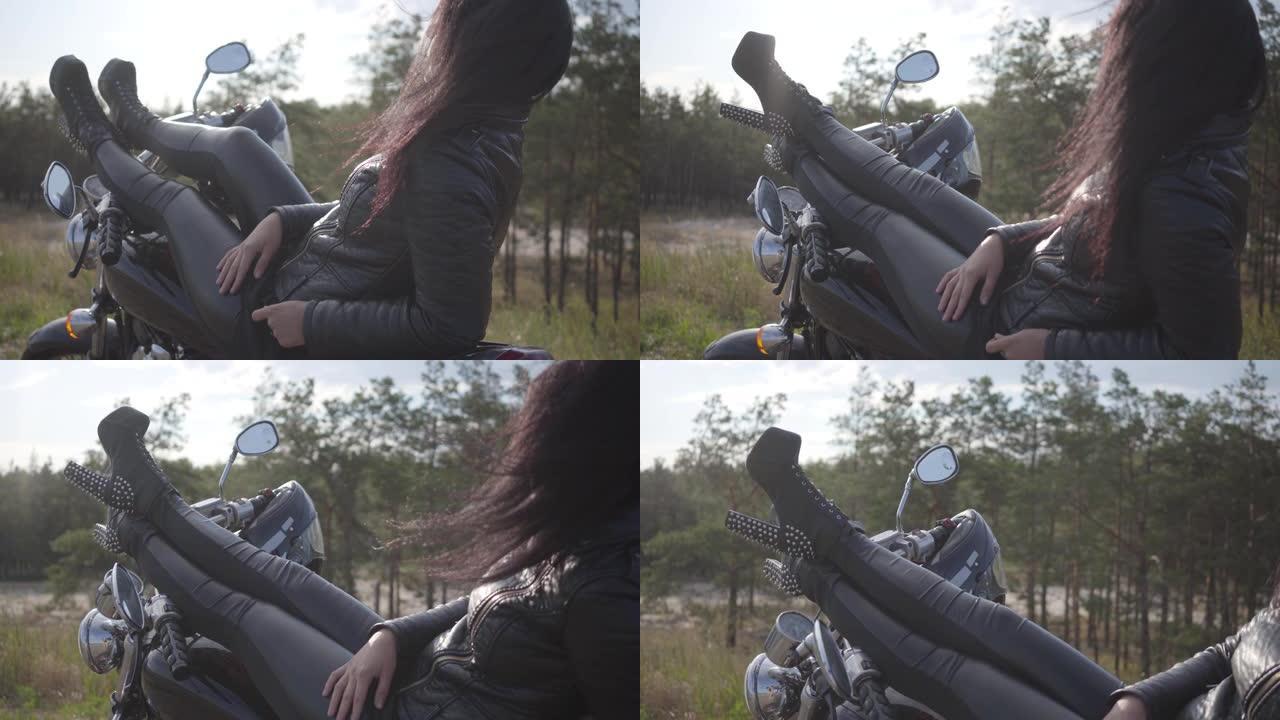 穿着黑色皮夹克和裤子的年轻白人女子躺在经典摩托车上。