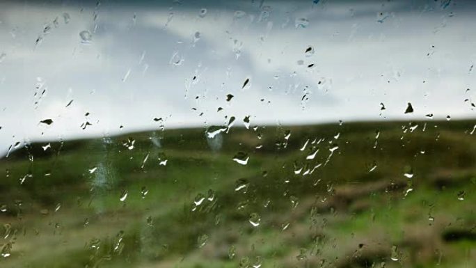 绿色山丘背景下的玻璃上的雨滴