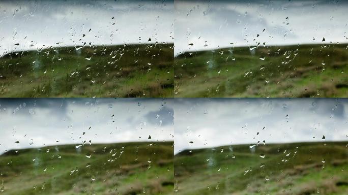 绿色山丘背景下的玻璃上的雨滴