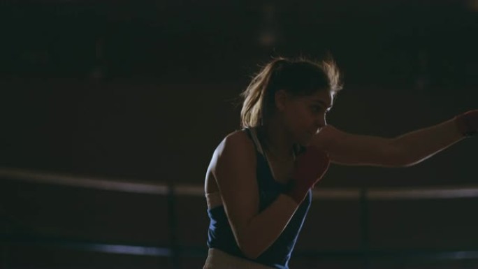 美丽性感的女人boxer动态打击直接进入相机，并在带有背光的黑暗背景下向前移动。Steadicam射
