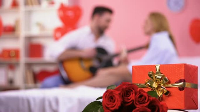 红色礼品盒和一束玫瑰特写，男性弹吉他浪漫旋律