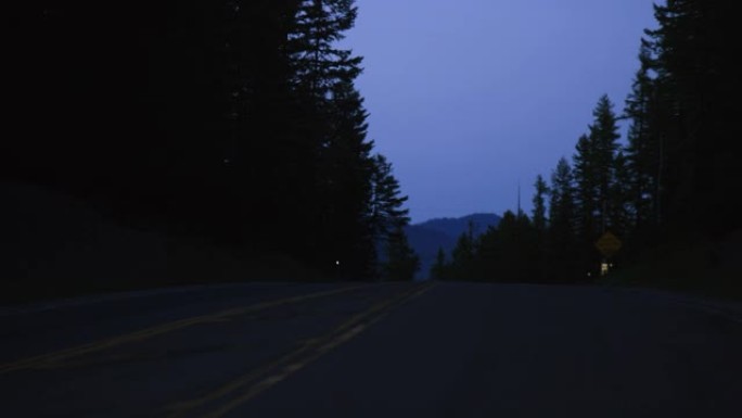 夜间在山中沿着树木环绕的道路行驶的车辆观点