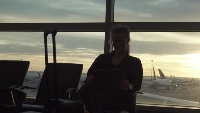 女人坐在机场休息室里，用平板电脑，窗户后面有飞机