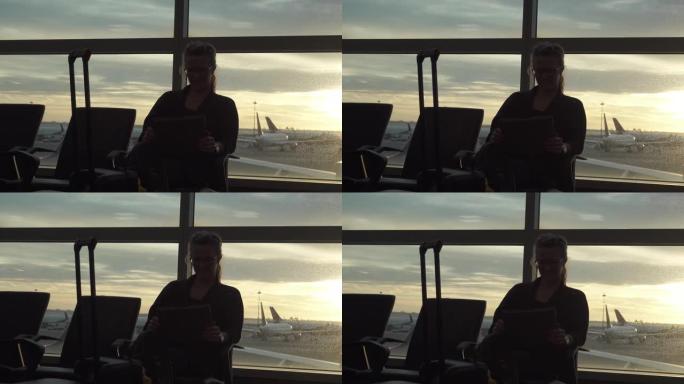 女人坐在机场休息室里，用平板电脑，窗户后面有飞机