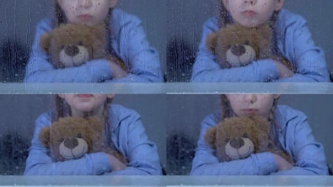 小女孤儿坐在雨窗后抱着泰迪熊做梦