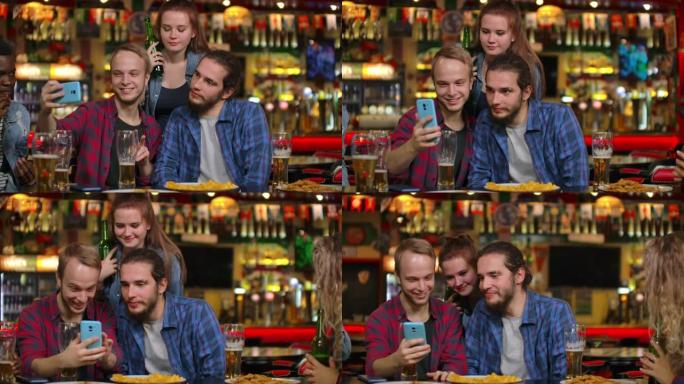 一群多民族的朋友在酒吧休息。朋友在酒吧用手机拍照，在手机上分享照片。在酒吧和朋友一起喝啤酒