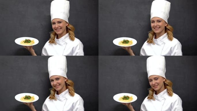 快乐的女厨师拿着面食和微笑的盘子，邀请去餐厅