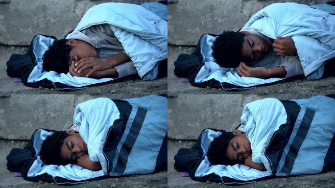 生病的黑人少年颤抖着被睡袋躺在街上的贫困覆盖
