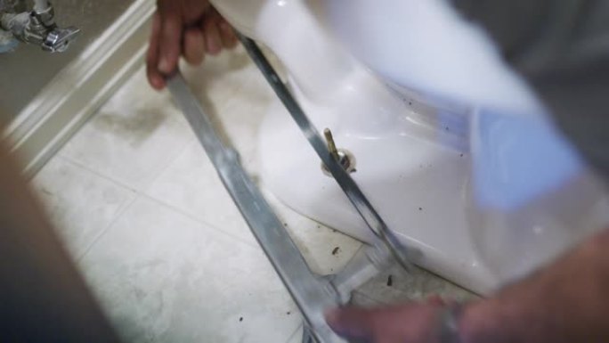 一名高加索修理工在室内家庭浴室中固定马桶时，使用锯子从法兰螺栓上切下多余的长度