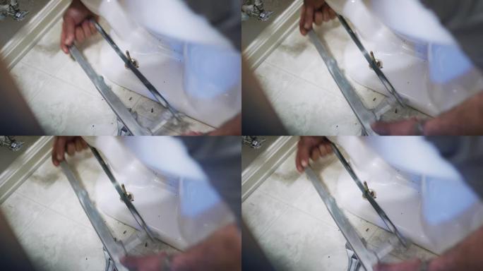 一名高加索修理工在室内家庭浴室中固定马桶时，使用锯子从法兰螺栓上切下多余的长度