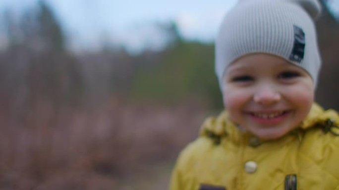 一个小美丽的微笑男孩的特写肖像，戴着帽子，戴着大睫毛，穿着黄色外套，直接看着相机。