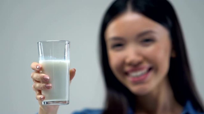 微笑的亚洲女孩向镜头展示一杯牛奶，健康的营养理念