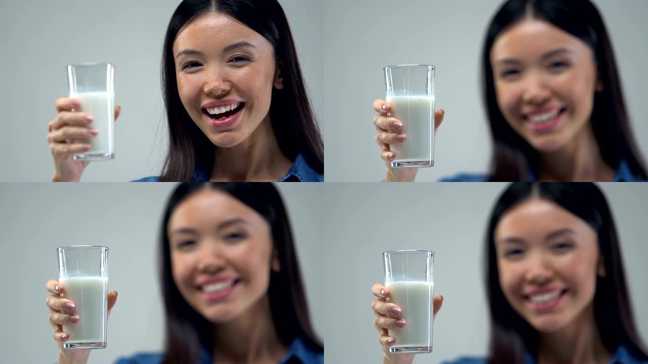 微笑的亚洲女孩向镜头展示一杯牛奶，健康的营养理念