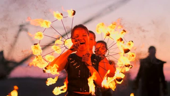 日落时分，在沙滩上放火的妇女跳舞，并以慢动作向美丽的天空展示技巧。