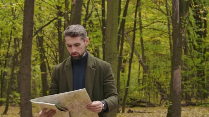 迷失的高加索游客站在树木之间的秋天森林中，看着地图和周围。自信的人正在寻找最好的路。电影院4k镜头P
