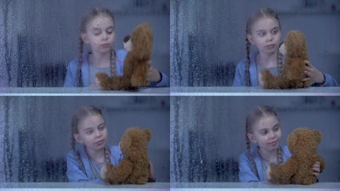 孤独的小女孩在雨天在家玩泰迪熊，没有朋友