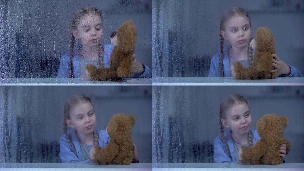 孤独的小女孩在雨天在家玩泰迪熊，没有朋友