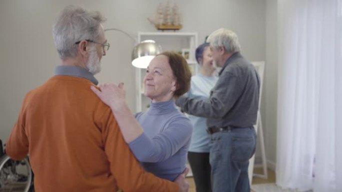 快乐的高加索高级男女在疗养院跳舞。孤独的老年退休人员在后台与志愿者共舞。享受夜晚的老养老金领取者。