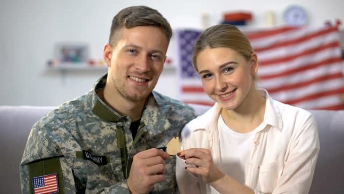 微笑的美国男士兵和他的妻子在照相机上展示木屋的标志