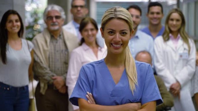 美丽的拉丁美洲护士双臂交叉对着镜头，而病人和医生站在背景下微笑