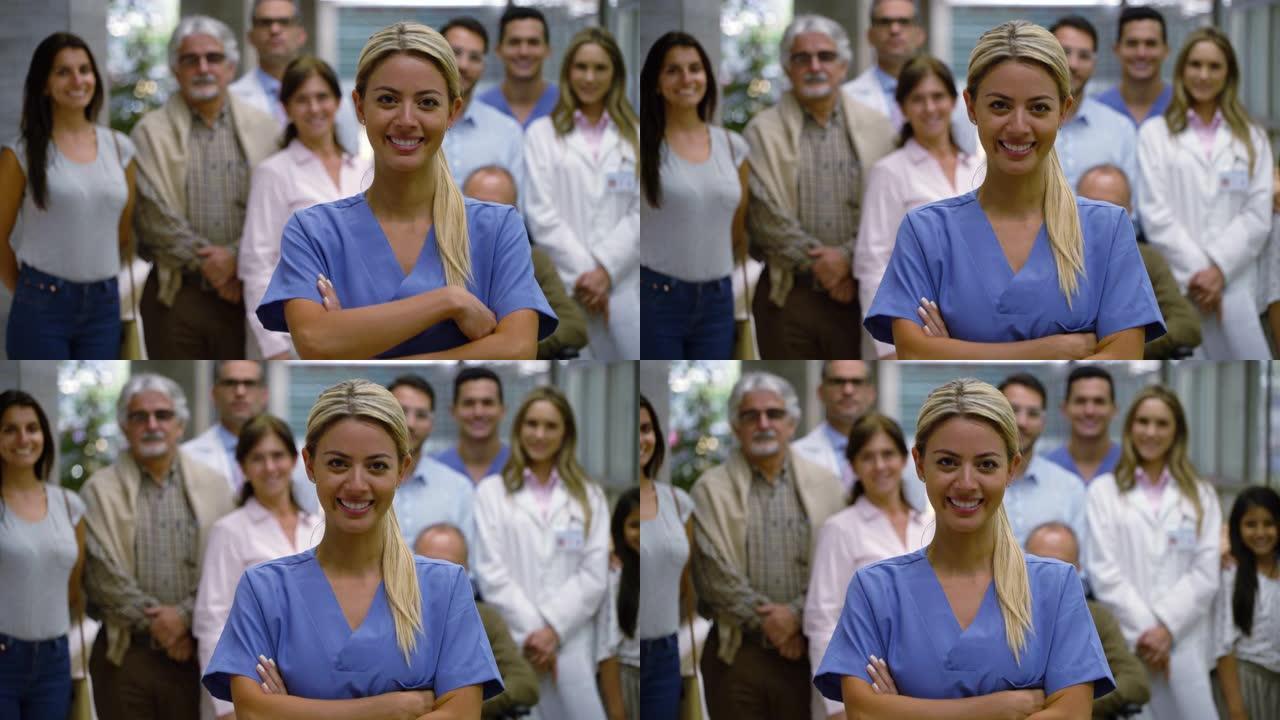 美丽的拉丁美洲护士双臂交叉对着镜头，而病人和医生站在背景下微笑