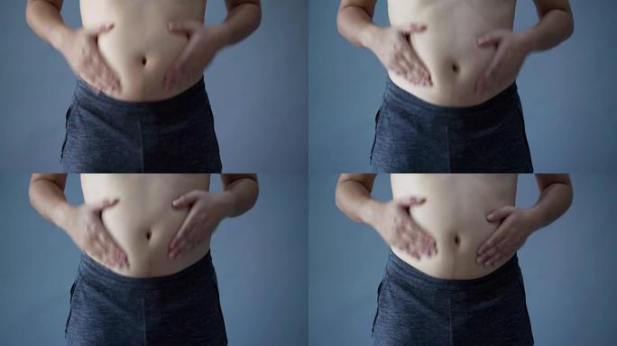 胖子超重，手握肥胖的腹部，在孤立的背景上，灰色的背景颜色。