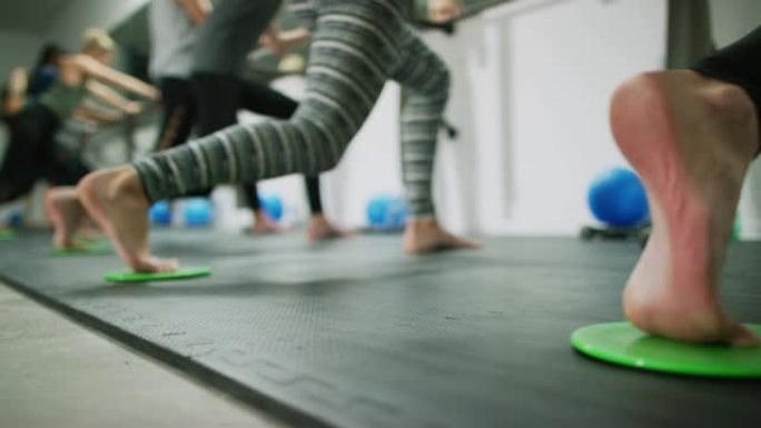二十多岁的多种族妇女在芭蕾舞棚上踩着核心滑块 (滑盘)，在健身室里冲刺