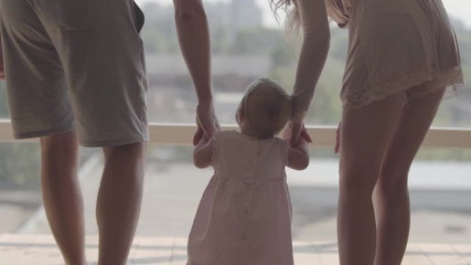 无法辨认的男人和女人在家里牵着可爱的婴儿的手走路。