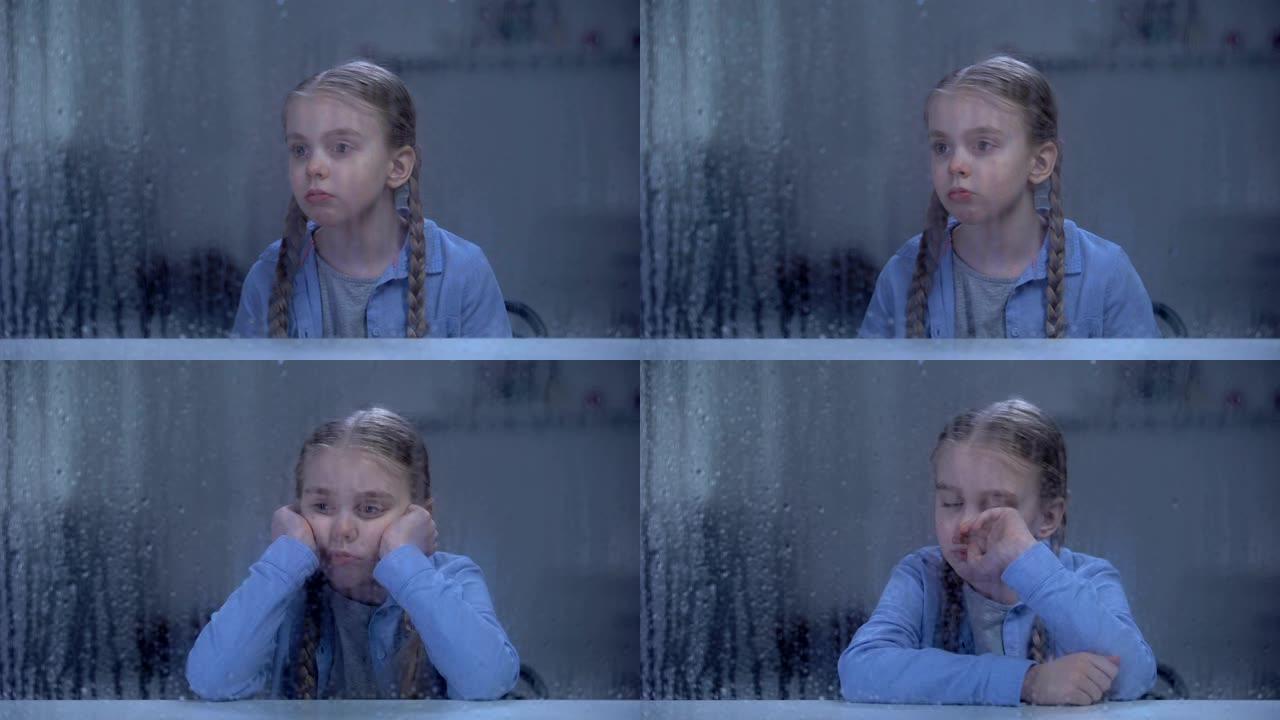 孤独的女孩在下雨的天气里看着窗户，等待父母下班