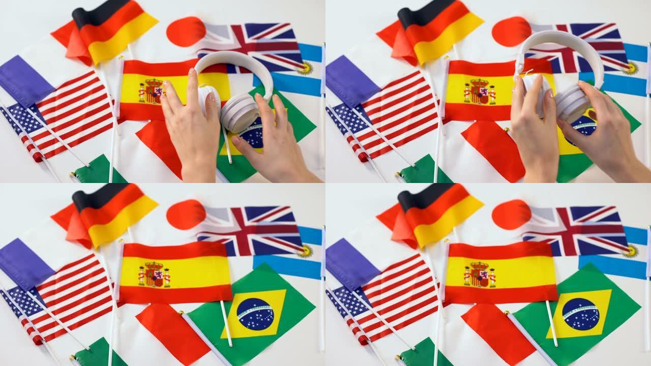 手拿耳机，不同国家的旗帜放在桌上，语言音频课程