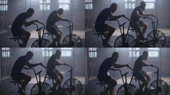 年轻活跃的两个人在健身房和教练一起锻炼空气自行车。两名男性在空中自行车上的训练与朋友鼓励。