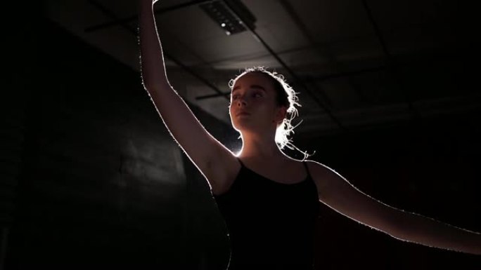 美丽的年轻芭蕾舞演员在黑暗中。黑色背景下的芭蕾舞练习。芭蕾舞演员美丽苗条的身材