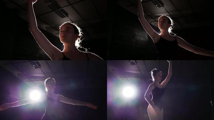 美丽的年轻芭蕾舞演员在黑暗中。黑色背景下的芭蕾舞练习。芭蕾舞演员美丽苗条的身材