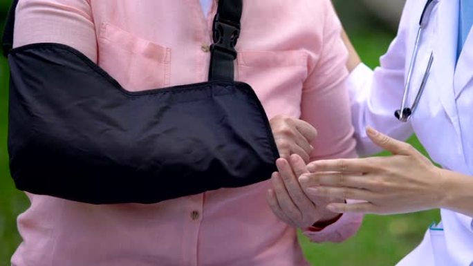 女性创伤专家在户外咨询手臂吊带的老年患者，治疗
