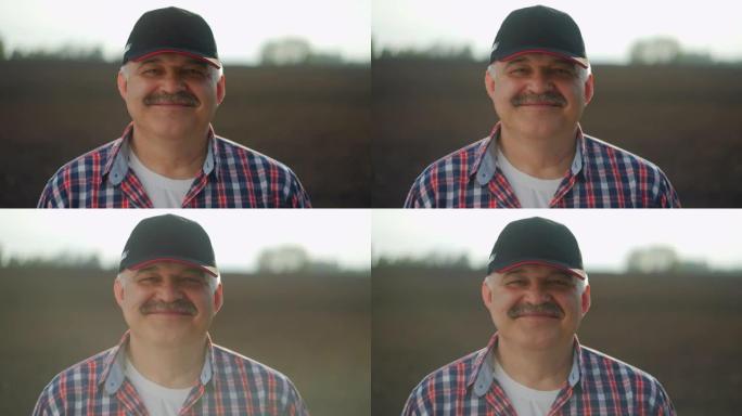 一个男性农民戴着棒球帽，在工作一天后看着相机微笑。