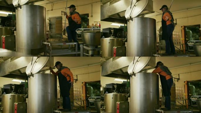 一名60多岁的白人妇女在商用厨房/制造设施中，用长桨在大型金属储罐中搅动脚手架并搅动液态食物