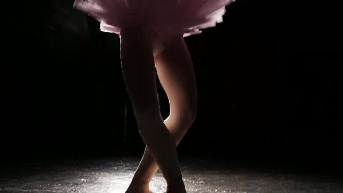 漂亮年轻优雅的芭蕾舞演员在工作室的黑色背景下，在她的尖头芭蕾舞鞋上跳舞。女人穿着芭蕾舞短裙和尖头鞋展