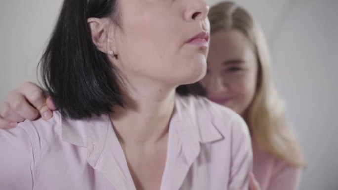 成年黑发白人妇女的特写肖像转向金发十几岁的女儿并拥抱她。母亲与孩子和睦相处。家庭关系，危机管理。