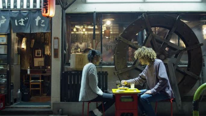 年轻的旅游夫妇坐在拥挤的东京餐厅外面