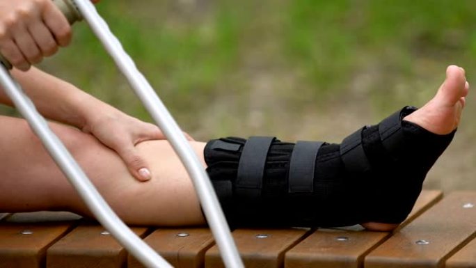 女拐杖患者在户外用步行支架按摩疼痛的腿