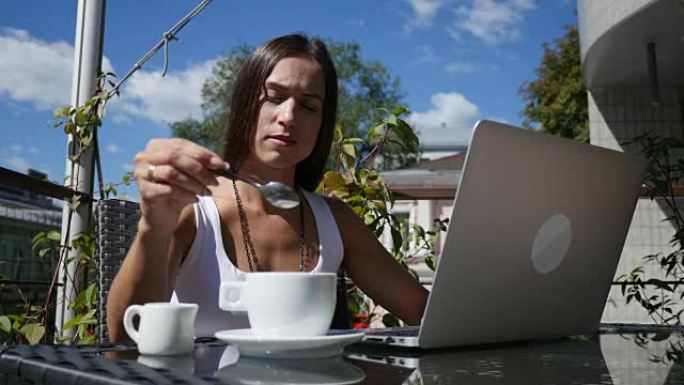 年轻女子在户外咖啡馆工作时在咖啡中倒牛奶